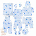A baby clothing set laid out on a white background, including a light blue long-sleeve top, matching footed pants, overalls, a cardigan, a bonnet, a bib, a hat, a muslin cloth, and booties, all printed with a blue heart pattern. A small plush bunny toy is