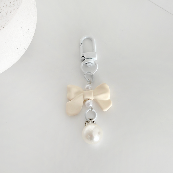 Cream bow keyring with pearl charm and silver clasp, displayed on a white background.