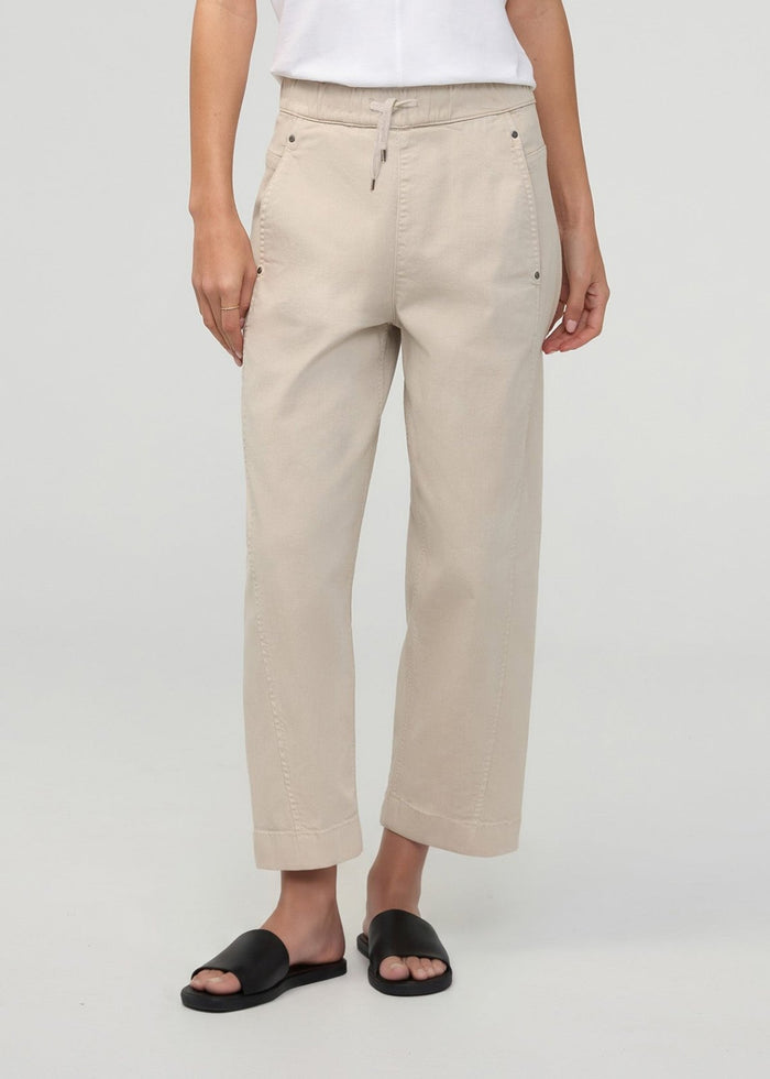 Sandstone pull-on pants with drawstring waist and side pockets, paired with a white shirt and black slides.