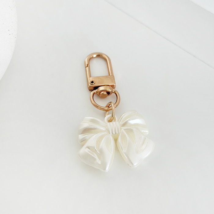 Gold keyring with a white pearl bow charm from Coconut Lane on a white surface.